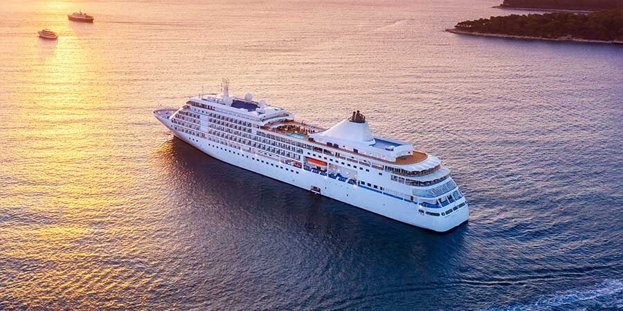 A large cruise ship sailing on calm waters during sunset with a colorful sky. - International Hotel School