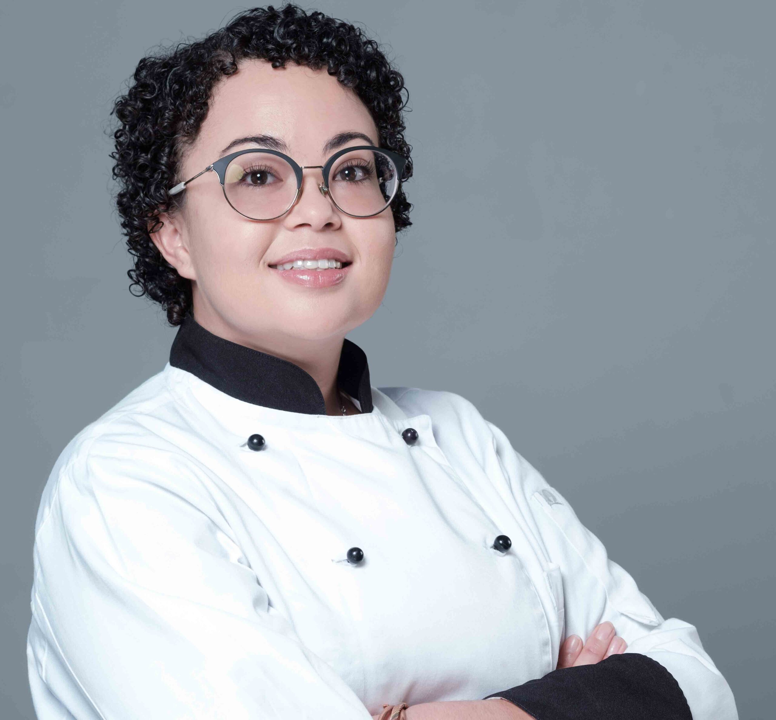 A chef wearing a white uniform and glasses, smiling with arms crossed. - International Hotel School