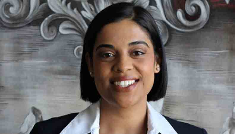 A professional woman smiling in a formal outfit against a decorative background. - International Hotel School