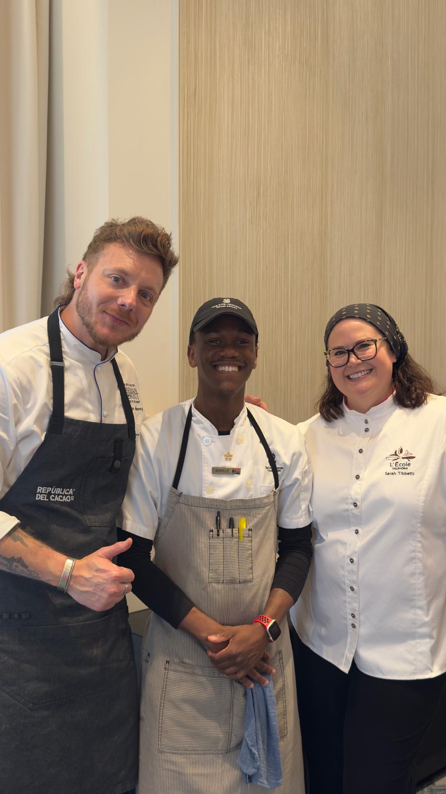 Three culinary professionals posing together in chef attire with kitchen tools visible. - International Hotel School