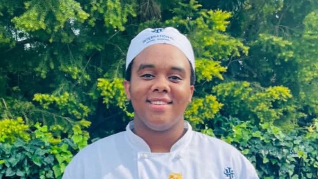 Culinary student wearing a chef uniform and hat from International Hotel School, smiling outdoors. - International Hotel School