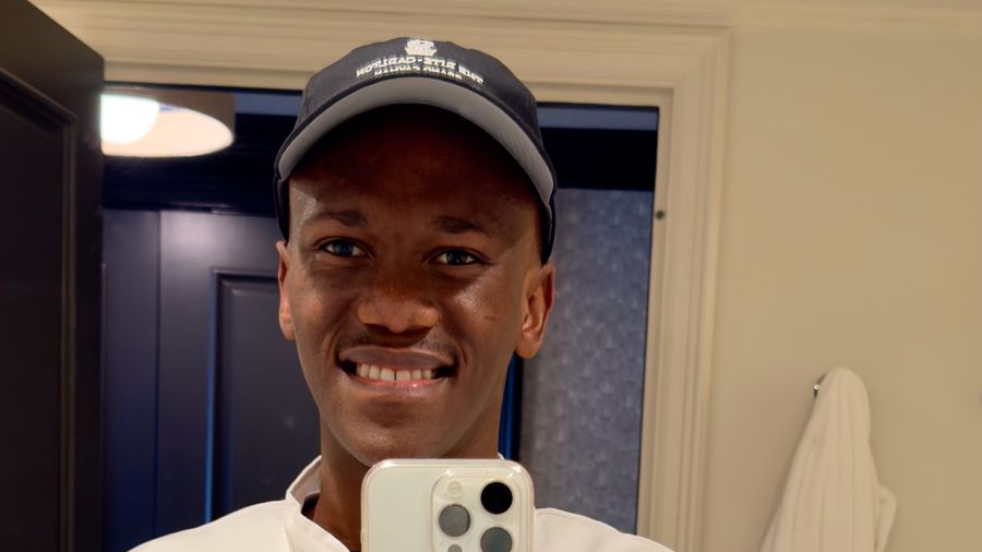 Individual smiling while holding a smartphone, wearing a cap with the International Hotel School logo. - International Hotel School