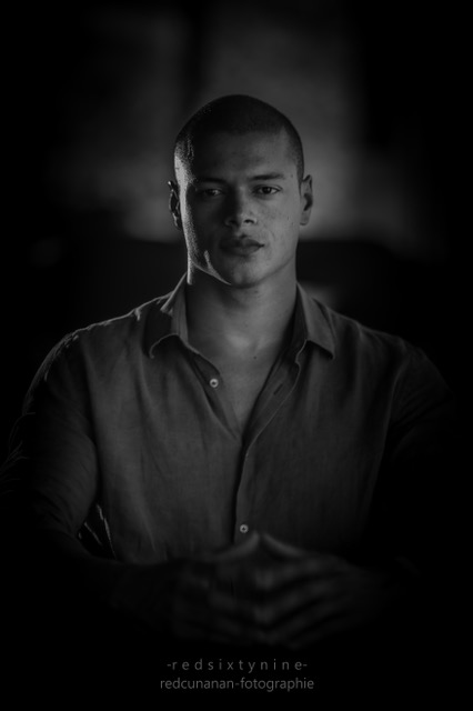 Black and white portrait of a young man with a serious expression, seated with hands clasped together. - International Hotel School