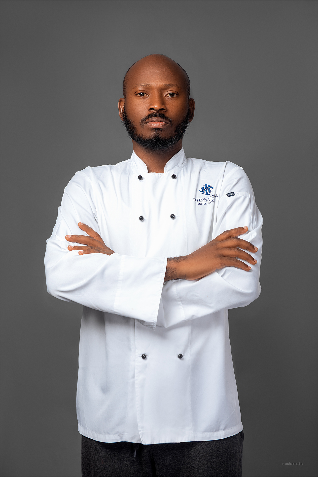 Chef wearing a white culinary uniform with arms crossed, displaying a professional demeanor. - International Hotel School