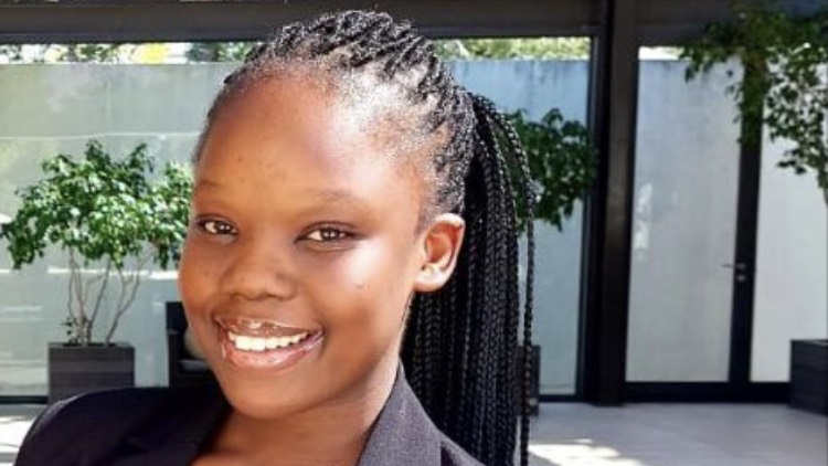 Young girl with braided hair smiling while wearing a black blazer in a bright setting. - International Hotel School
