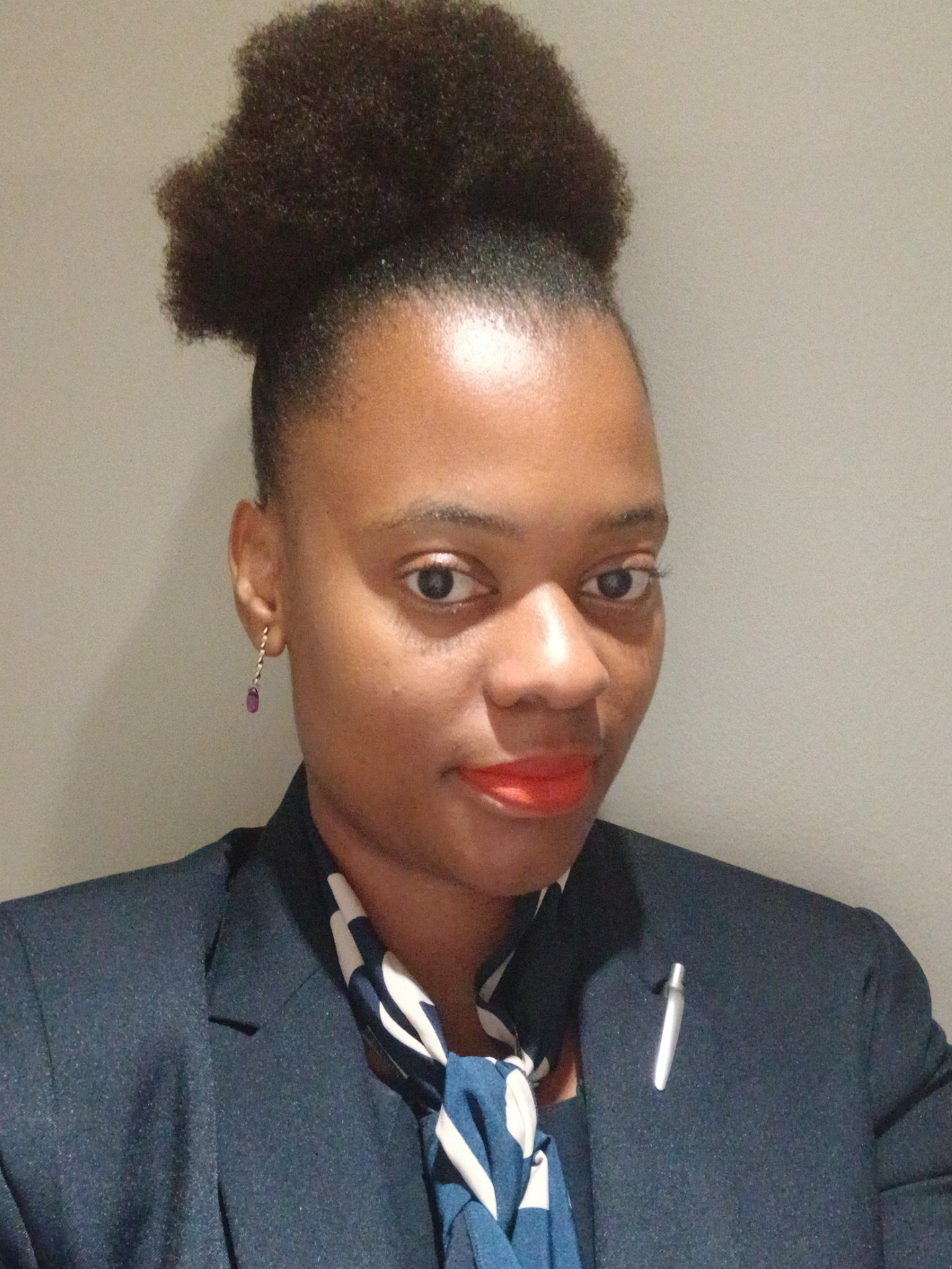 A woman with natural hair styled in a puff, wearing a business suit and a patterned scarf. - International Hotel School