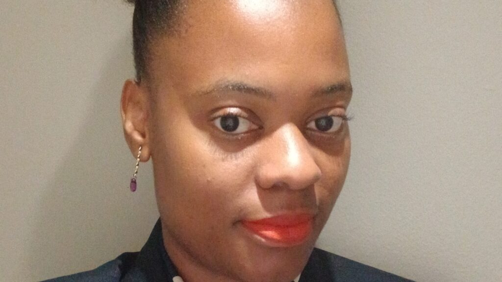 Close-up portrait of a woman with earrings and bright orange lipstick, smiling softly. - International Hotel School