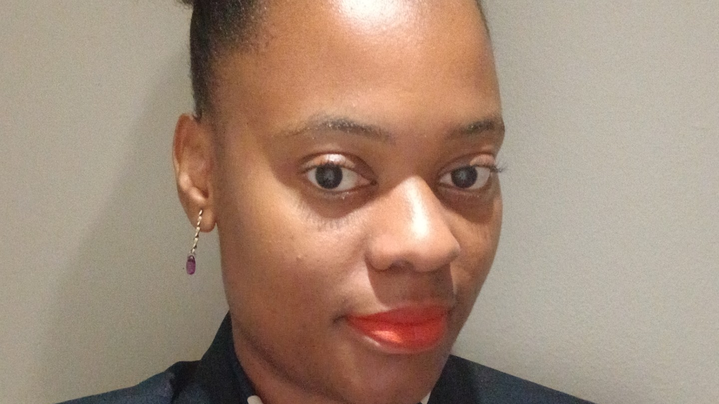 Close-up portrait of a woman with earrings and bright orange lipstick, smiling softly. - International Hotel School