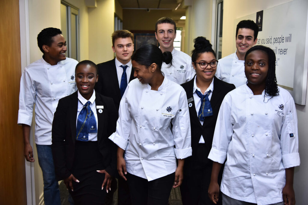 A group of students wearing chef uniforms and formal attire walking together in a hallway. - International Hotel School