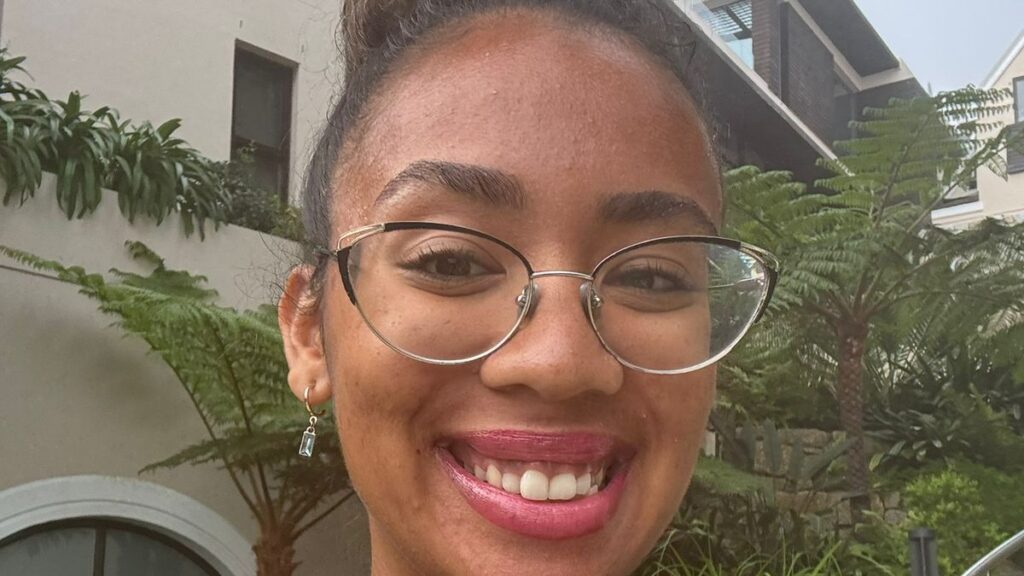Young woman with glasses and a bun hairstyle smiling outdoors in a garden setting. - International Hotel School