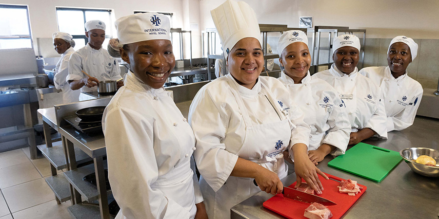 Group of culinary students in white uniforms preparing food in a professional kitchen setting. - International Hotel School